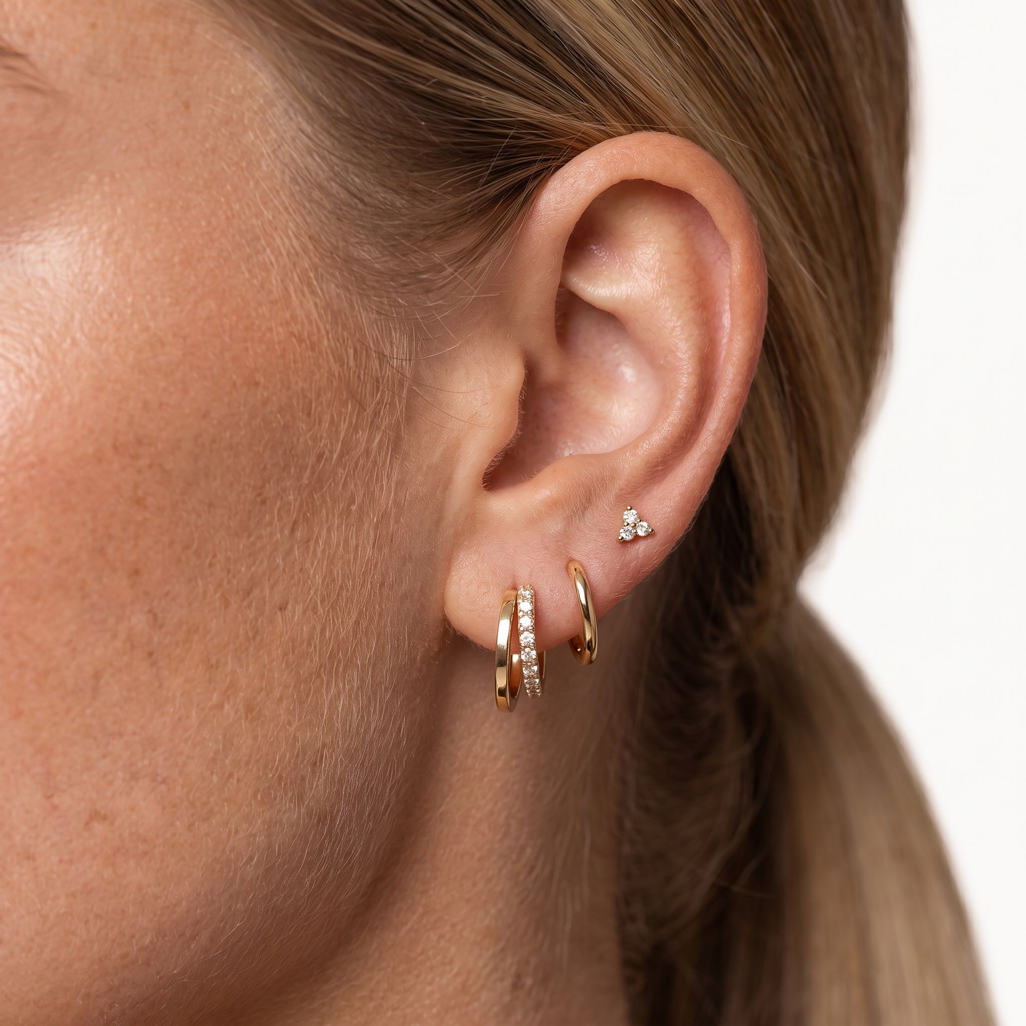 Gold-tone clover hoop earrings and crystal stud worn stacked in one ear