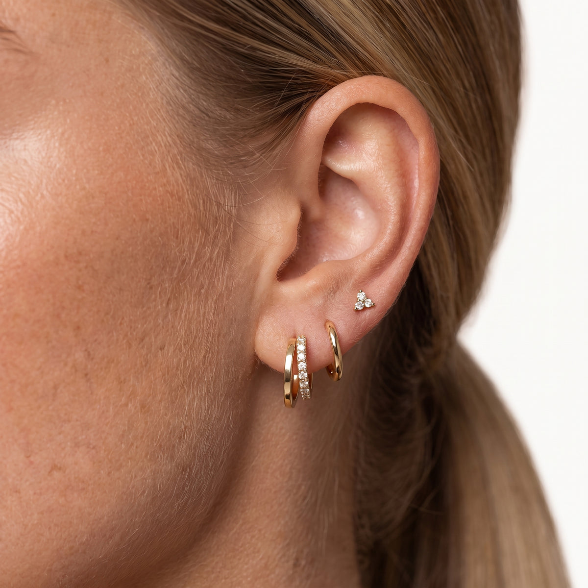 Gold-tone clover hoop earrings and crystal stud worn stacked in one ear