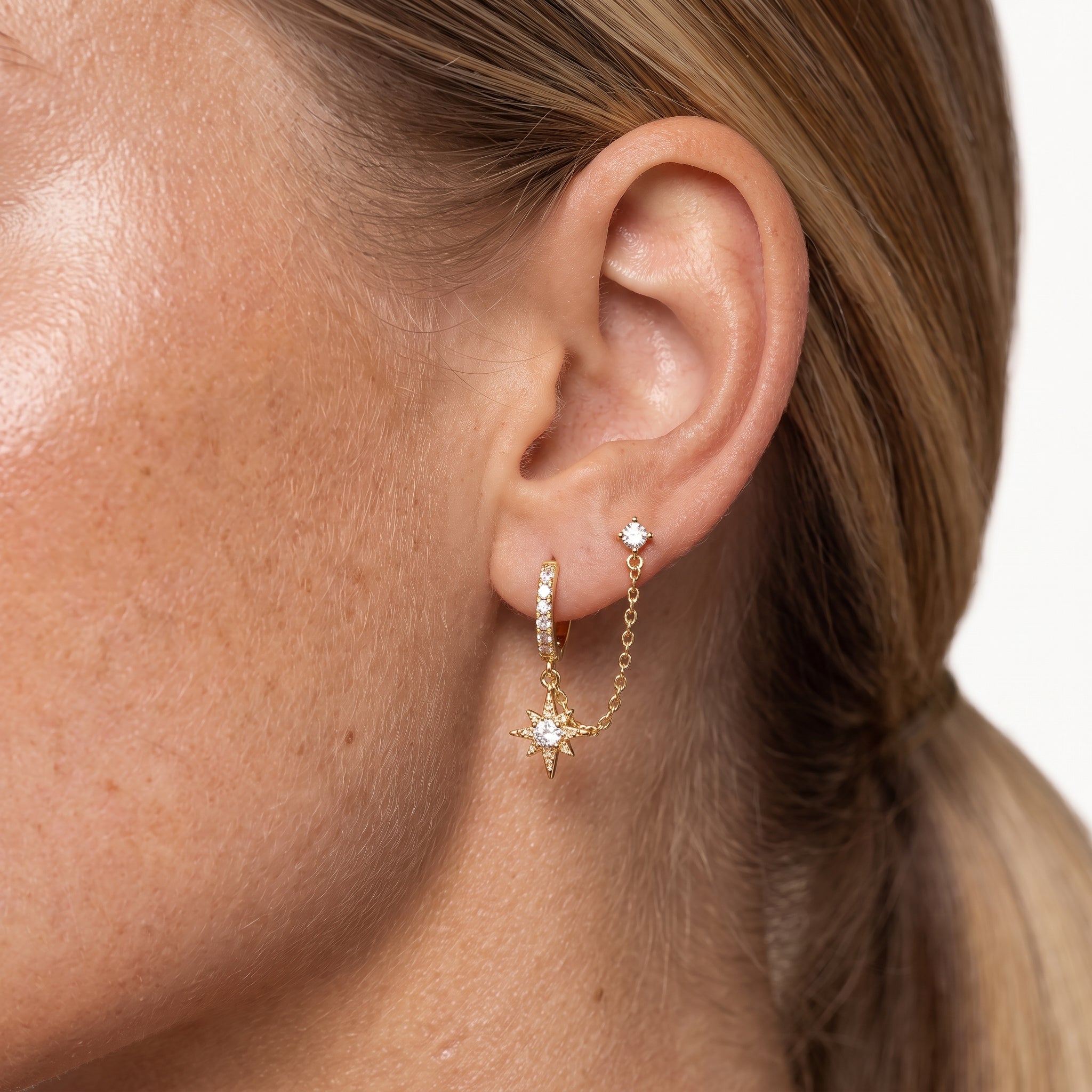 Gold-tone chained huggie earring worn with the stud in a second piercing