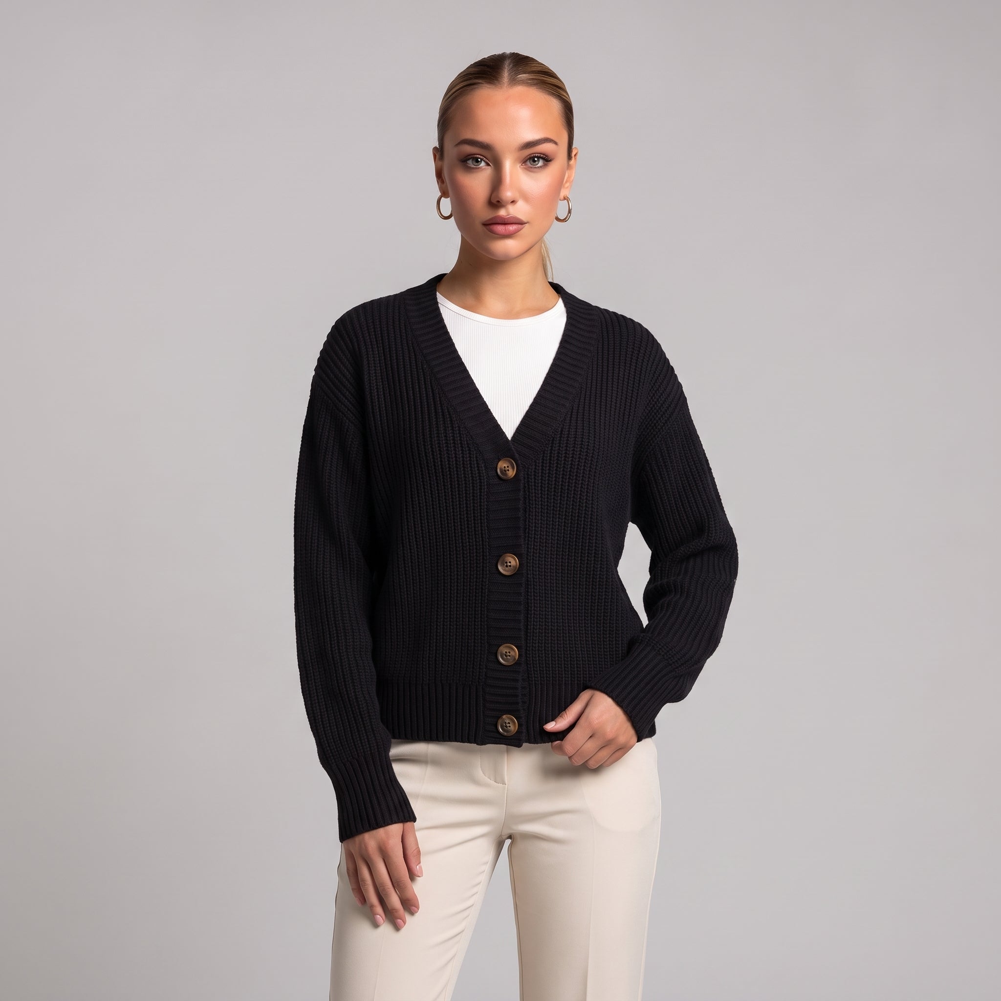 Black chunky knit cardigan worn open over a white top, half body front view