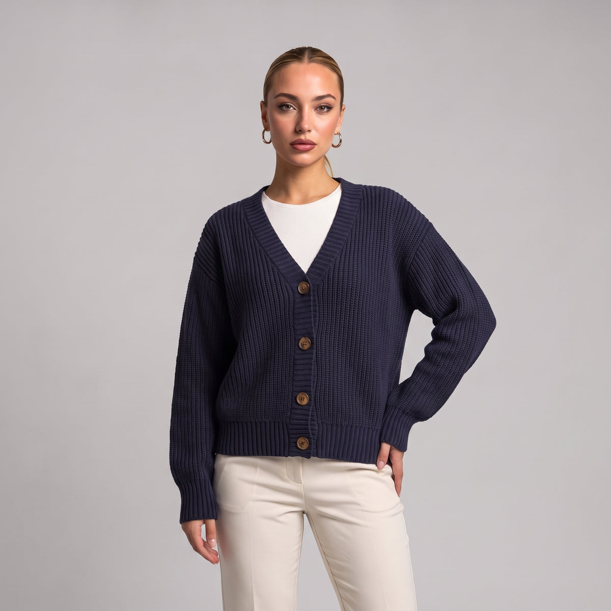 Navy chunky knit cardigan worn open over a white top, half body front view