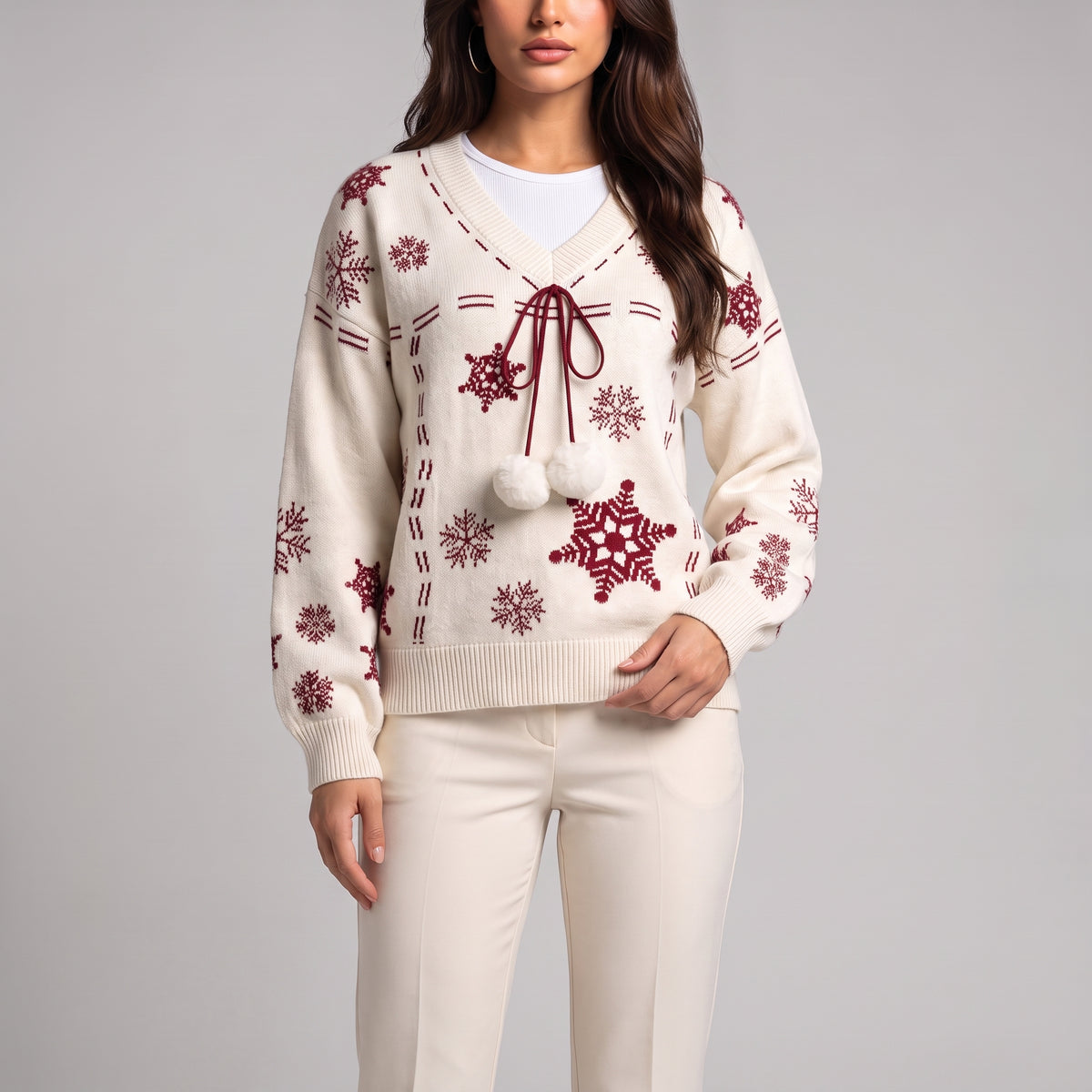 Close-up of white knit jumper with red snowflakes, red tie cord and white pom poms
