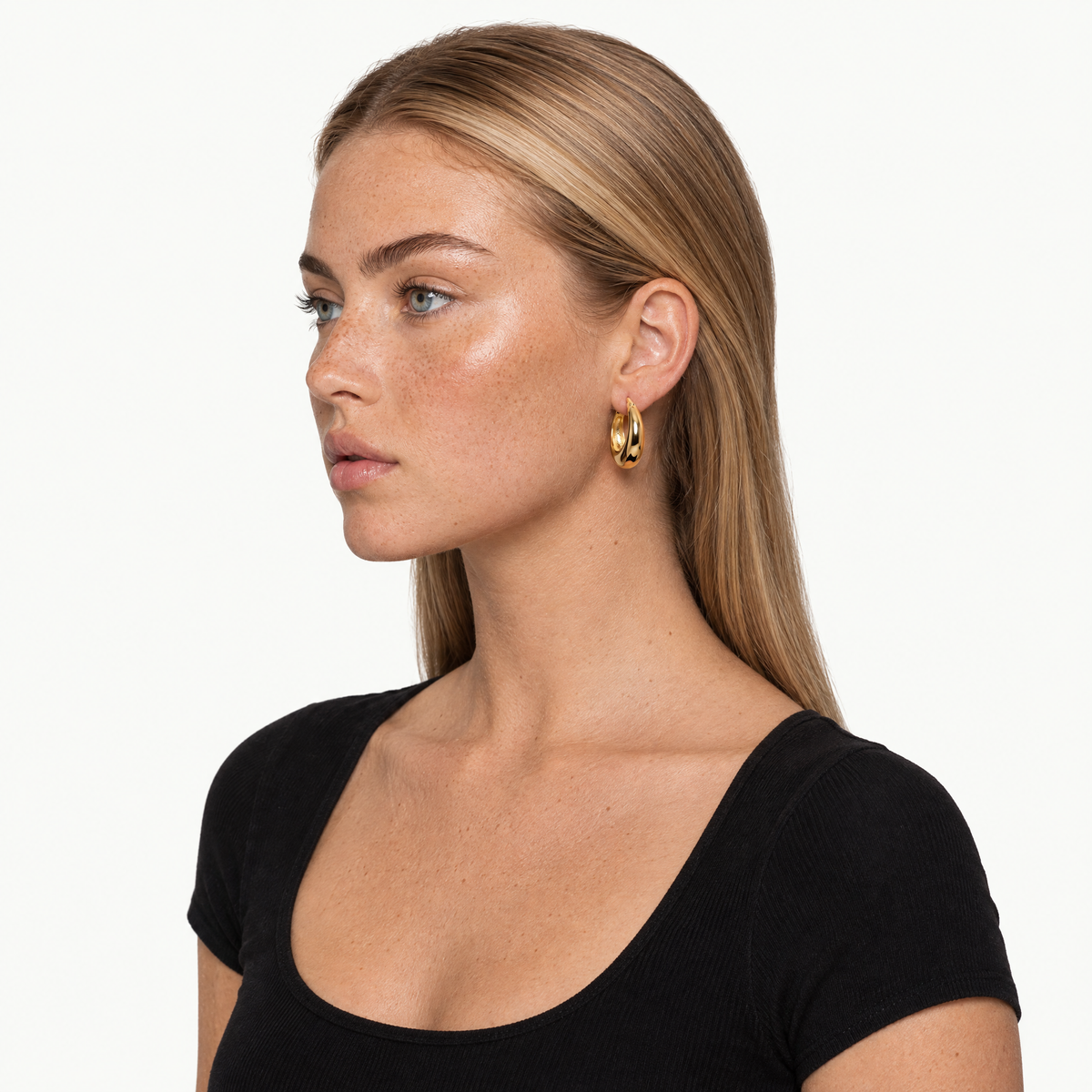 Gold-tone chunky tapered hoop earring worn by a model, shown with head and shoulders