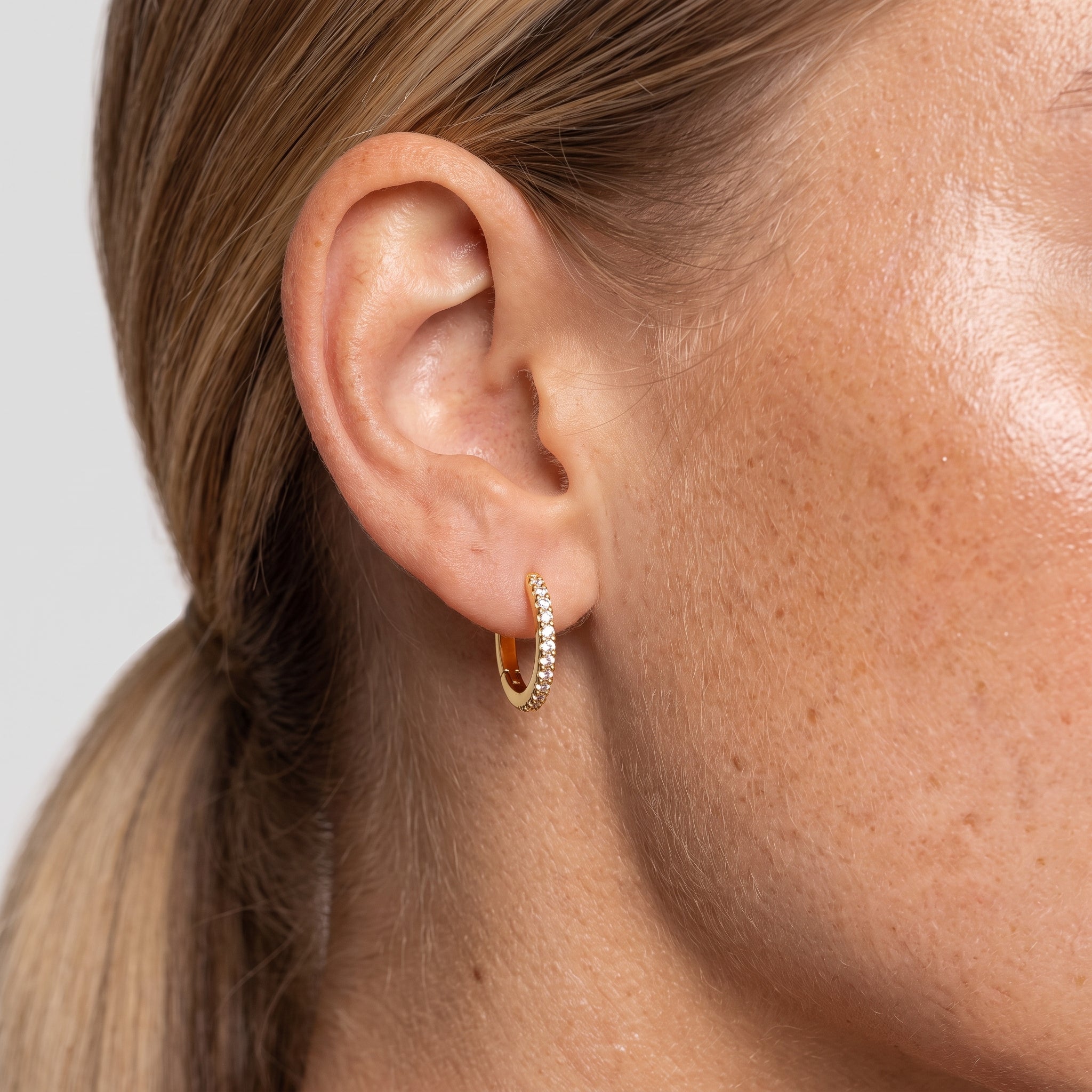 Gold-tone crystal huggie hoop earring worn in the ear