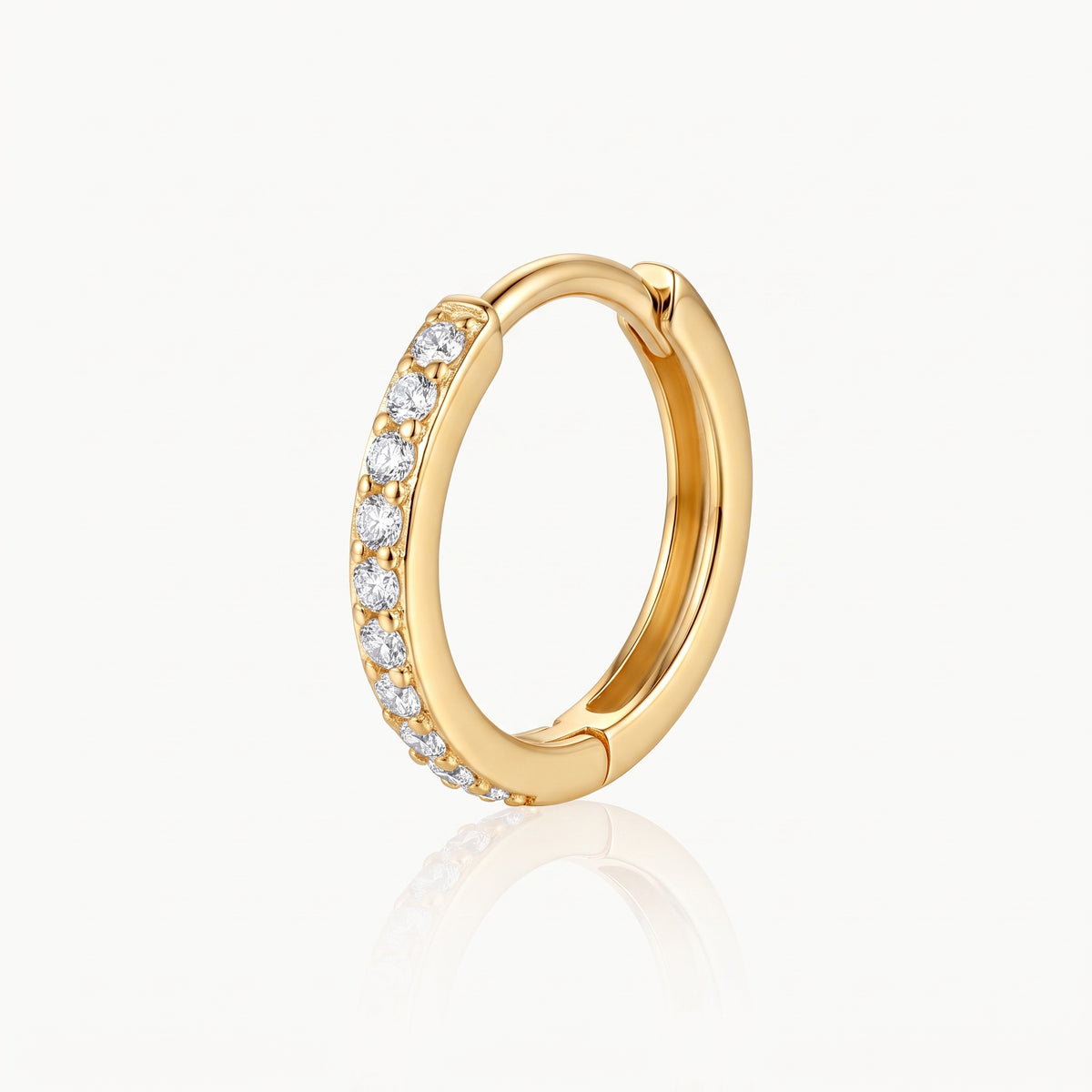 Close-up of a gold-tone huggie hoop earring with a row of clear crystal stones and hinged closure