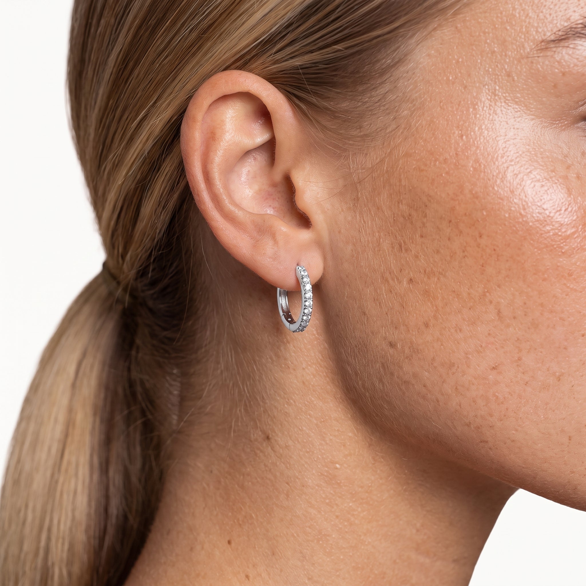 Silver-tone crystal huggie hoop earring worn in the ear
