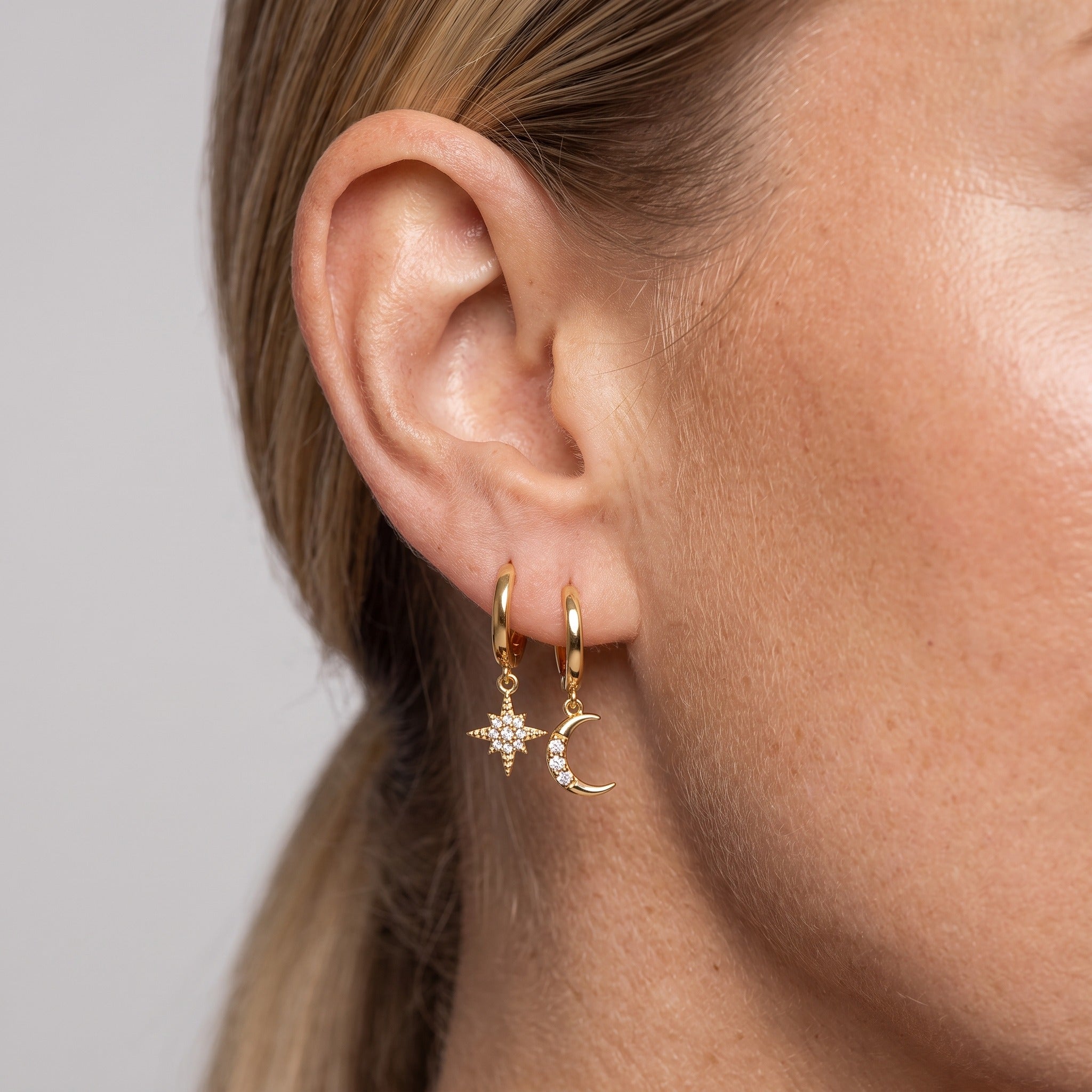 Gold-tone moon and star huggie earrings worn on the ear