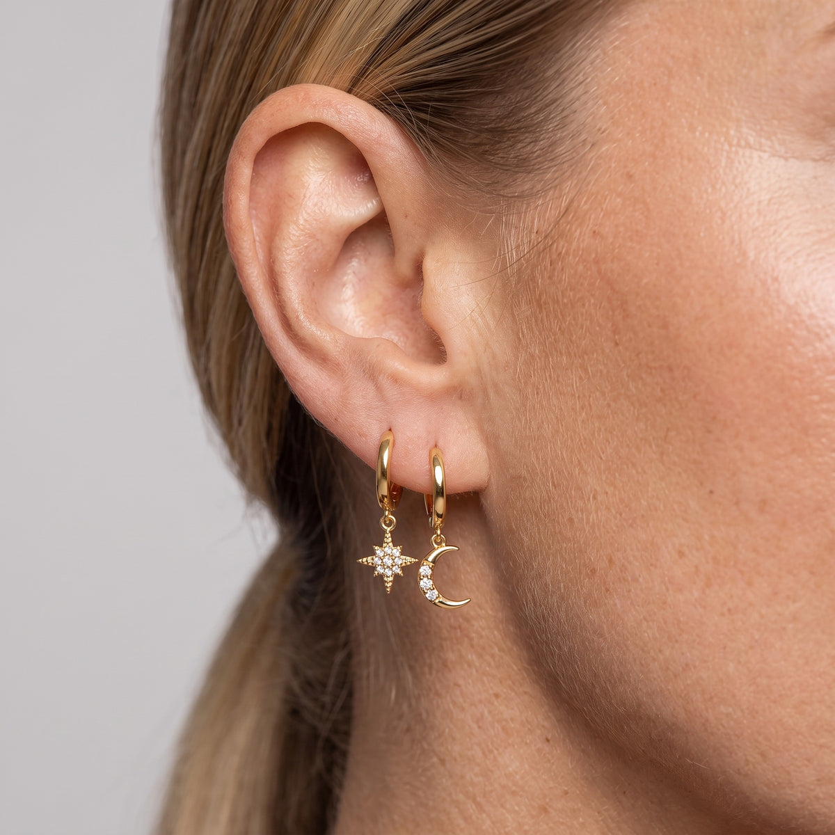 Gold-tone moon and star huggie earrings worn on the ear