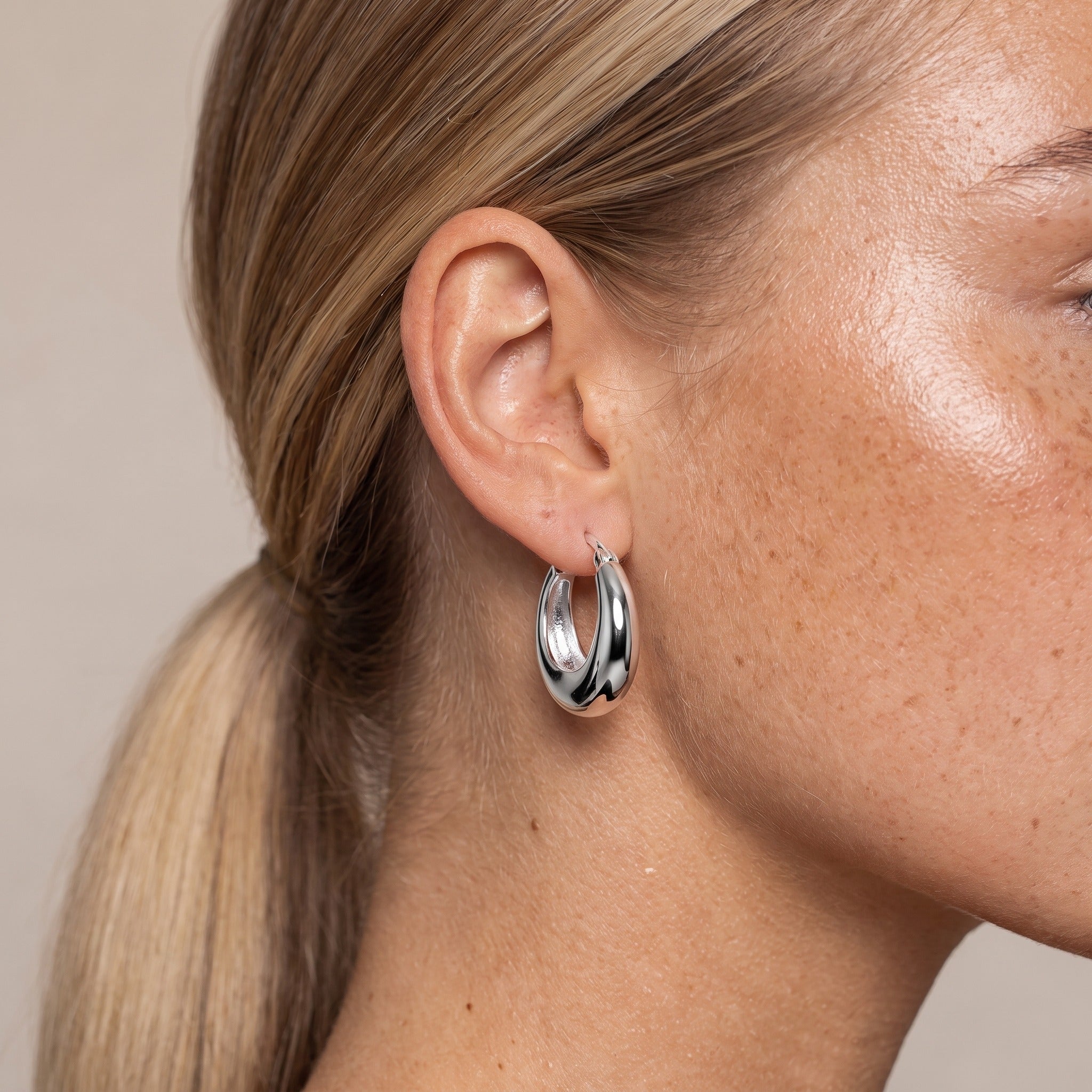 Silver-tone chunky tapered hoop earring worn on the ear