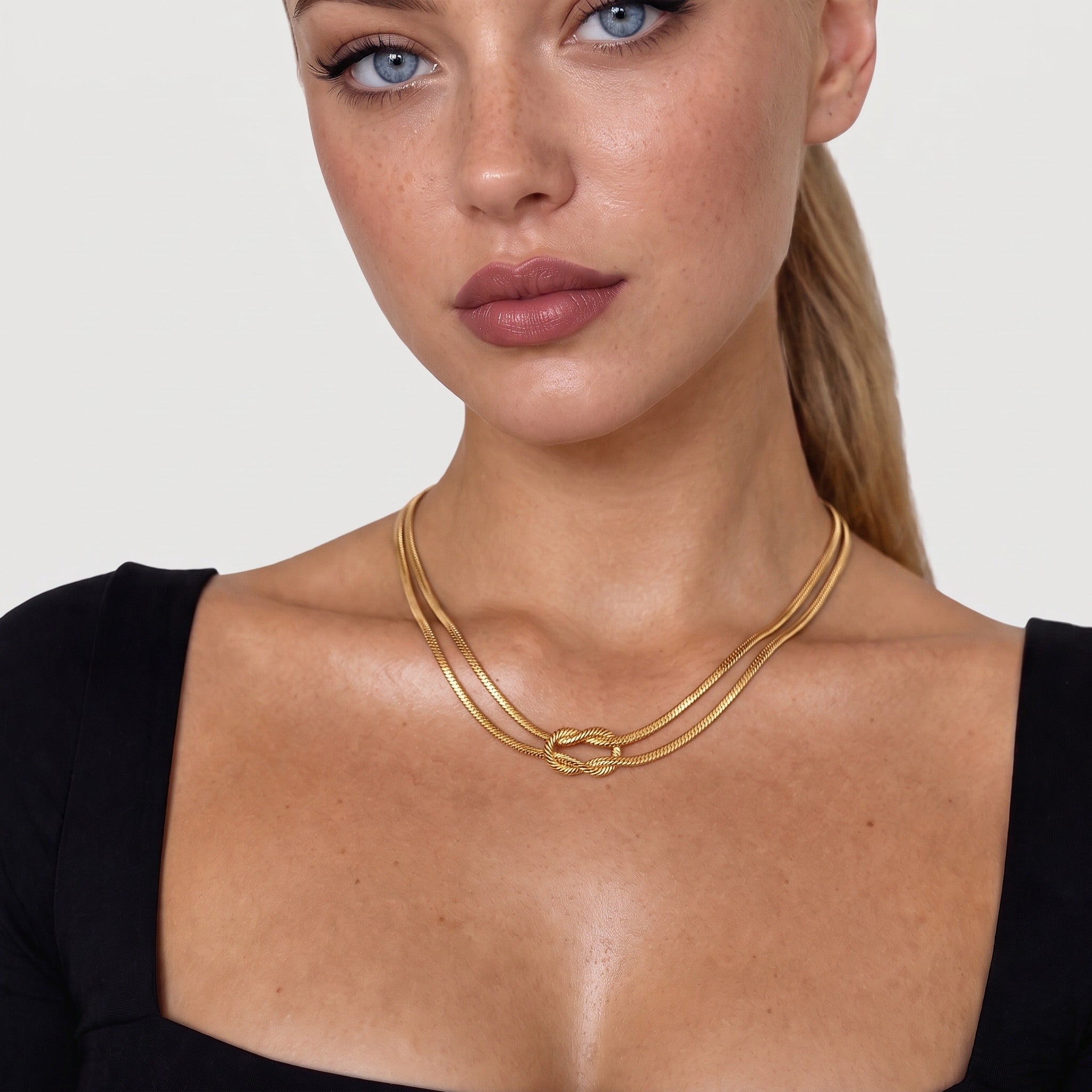 Gold-tone knot necklace worn at the collarbone