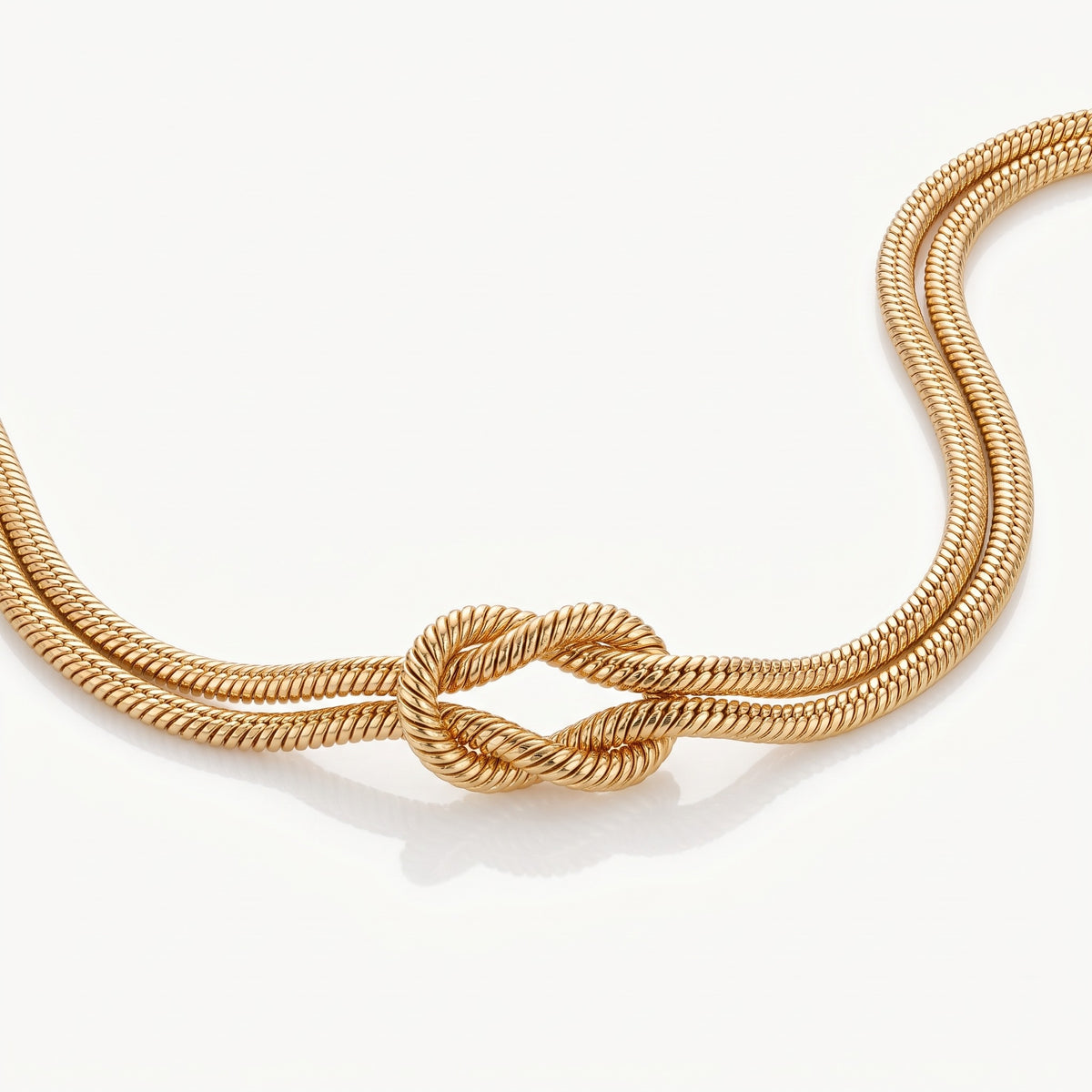 Gold-tone double snake chain crossing into a knot, seen from above