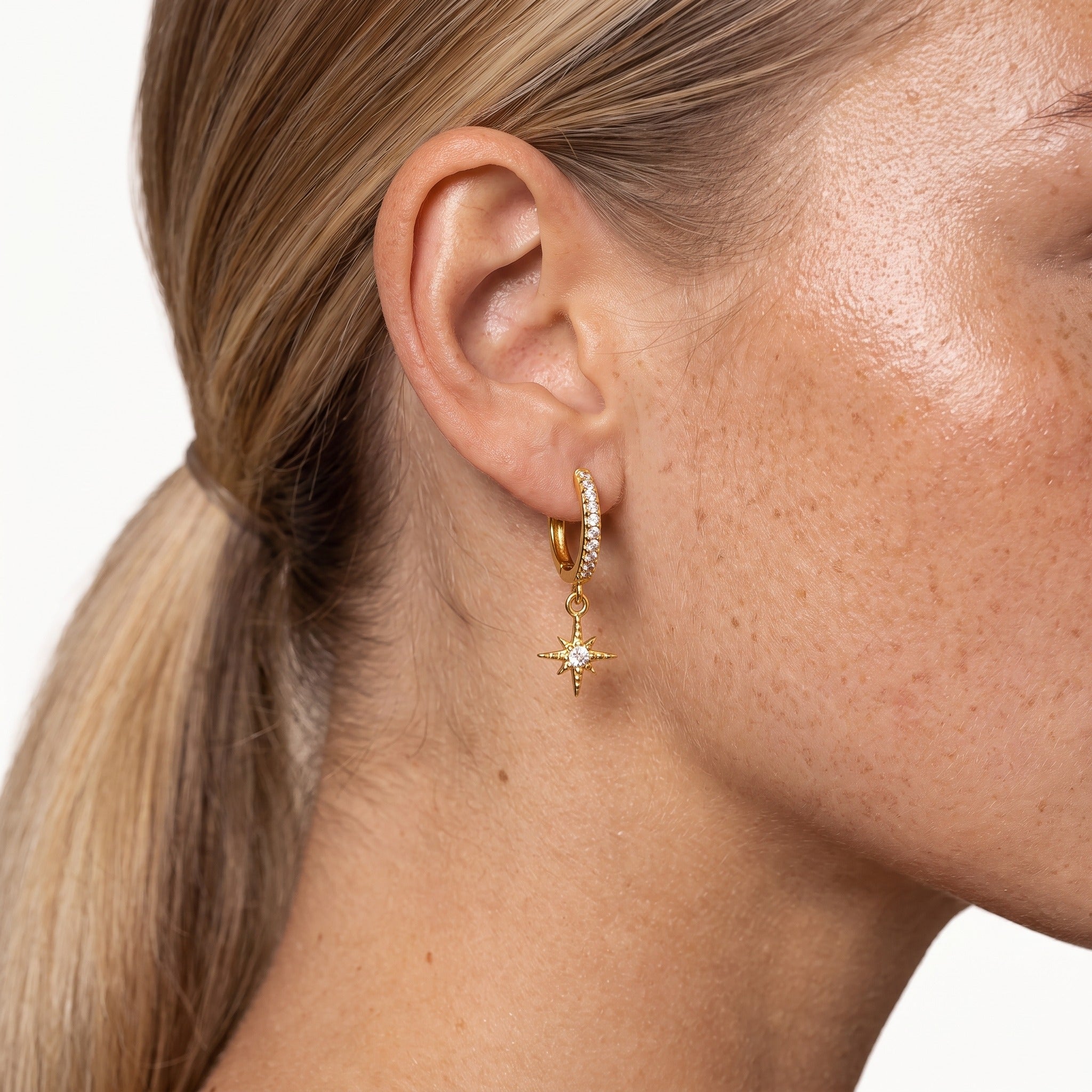 Gold-tone star charm huggie hoop earrings, worn on the ear