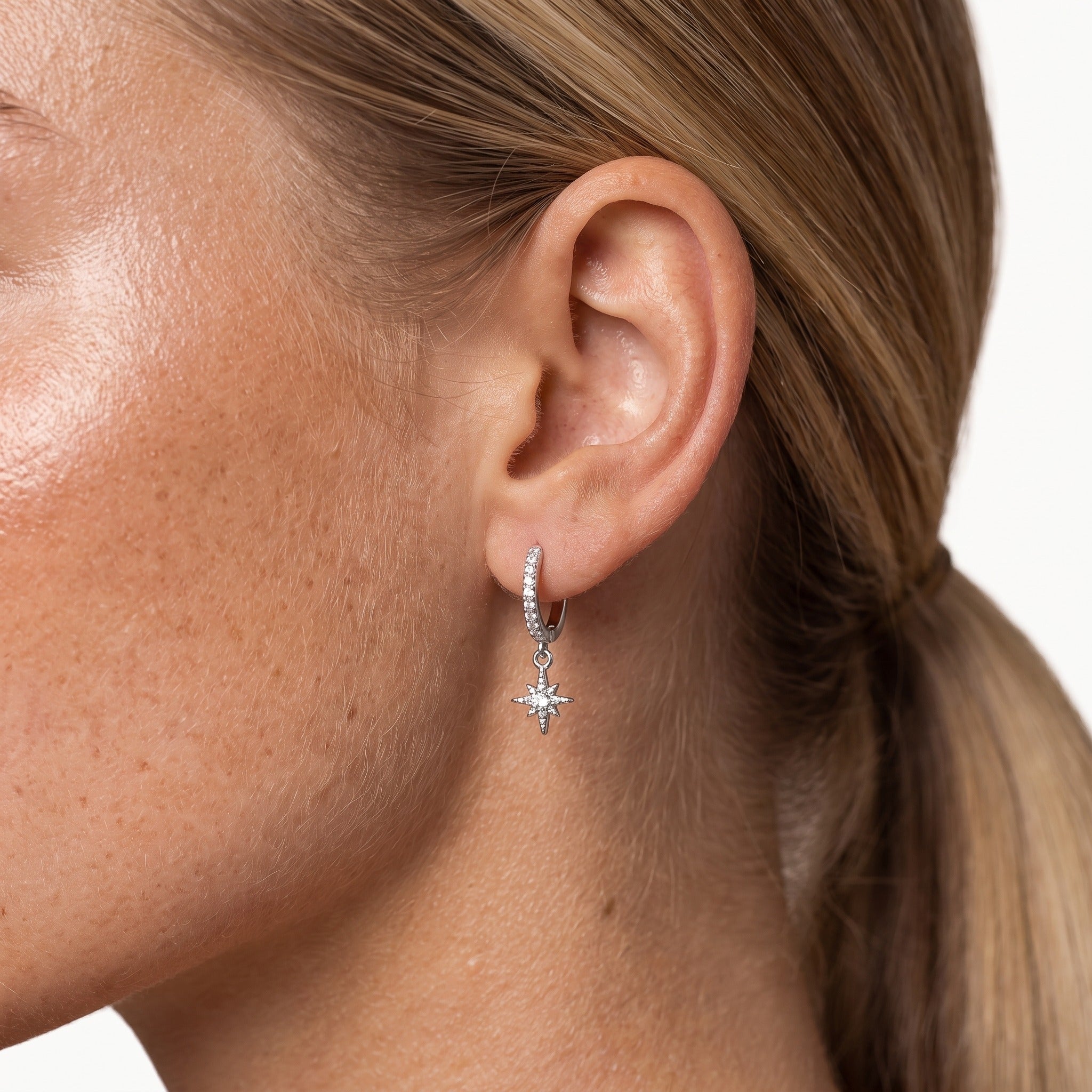 Silver-tone star charm huggie hoop earring, worn on the ear
