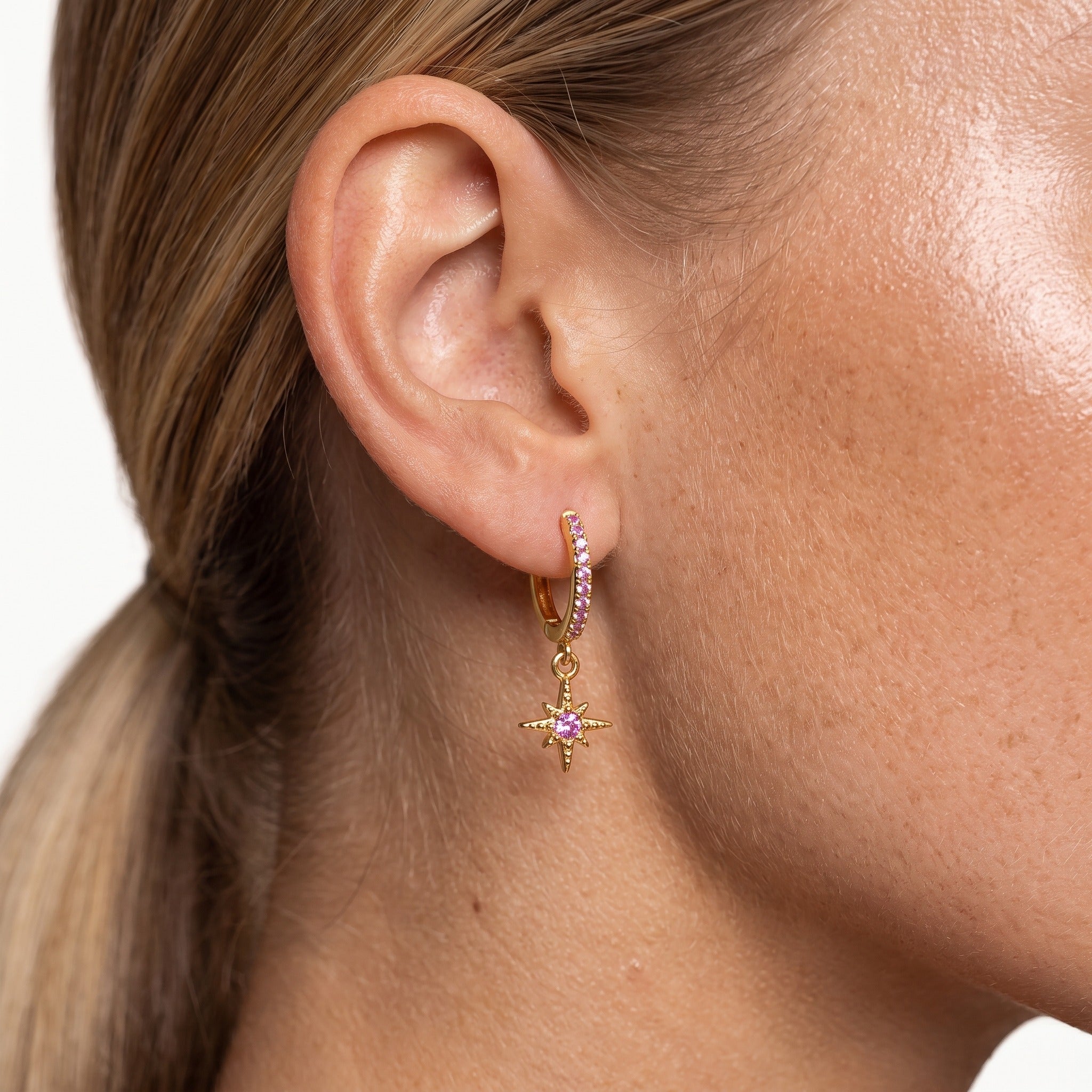 Gold-tone star charm huggie hoop earring with pink crystals, worn on the ear