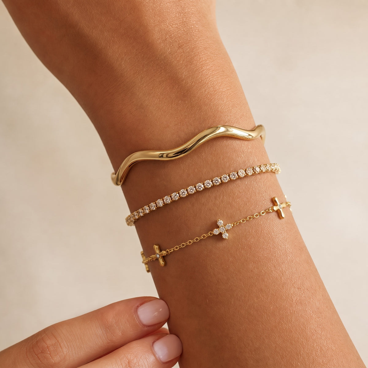 Gold-tone cross charm bracelet with crystals, stacked on the forearm