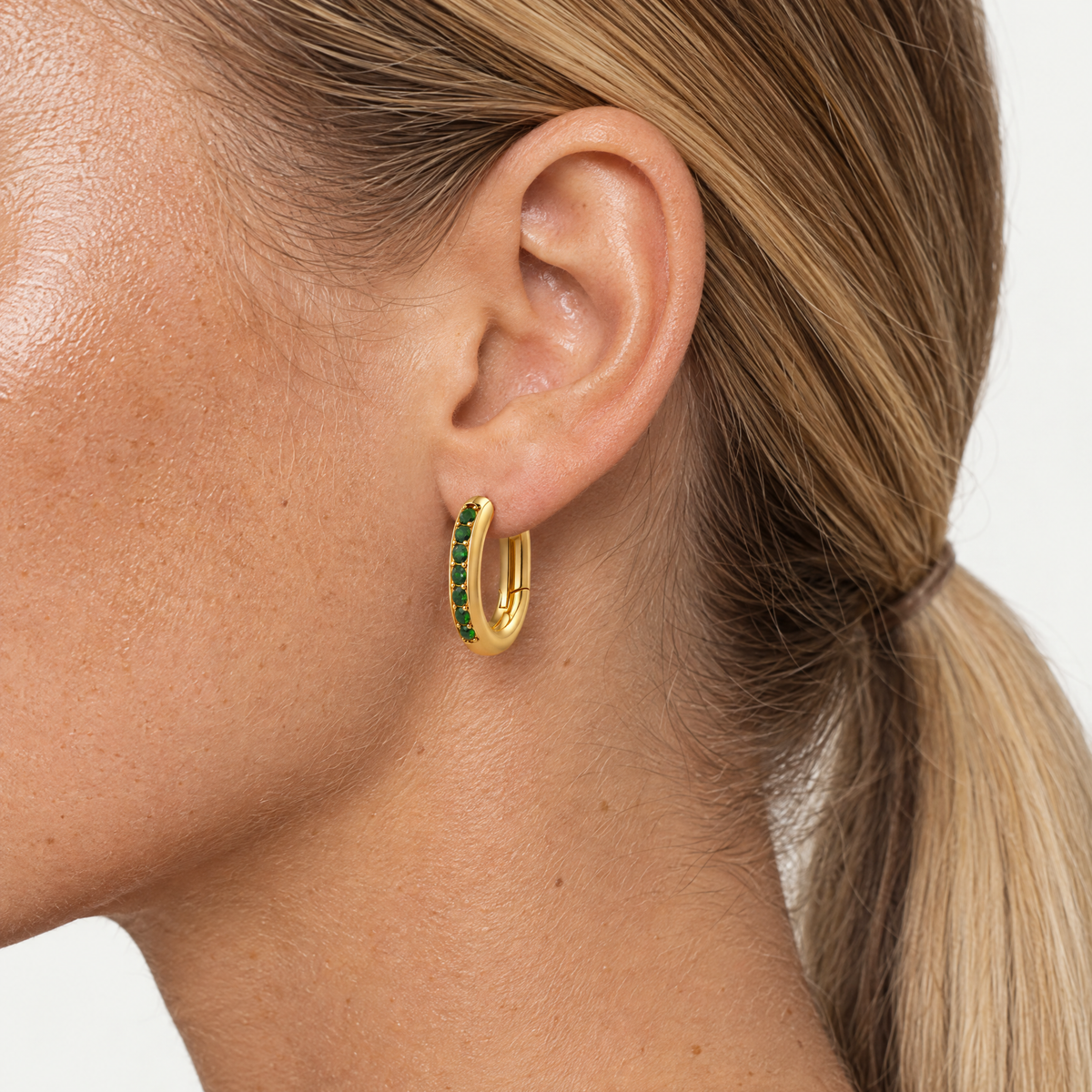 Close up of an ear wearing the oval huggie hoop with green stones