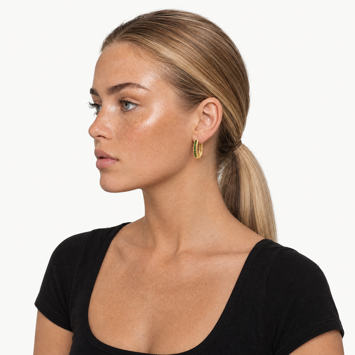 Model wearing the gold-tone oval huggie hoops with green stones