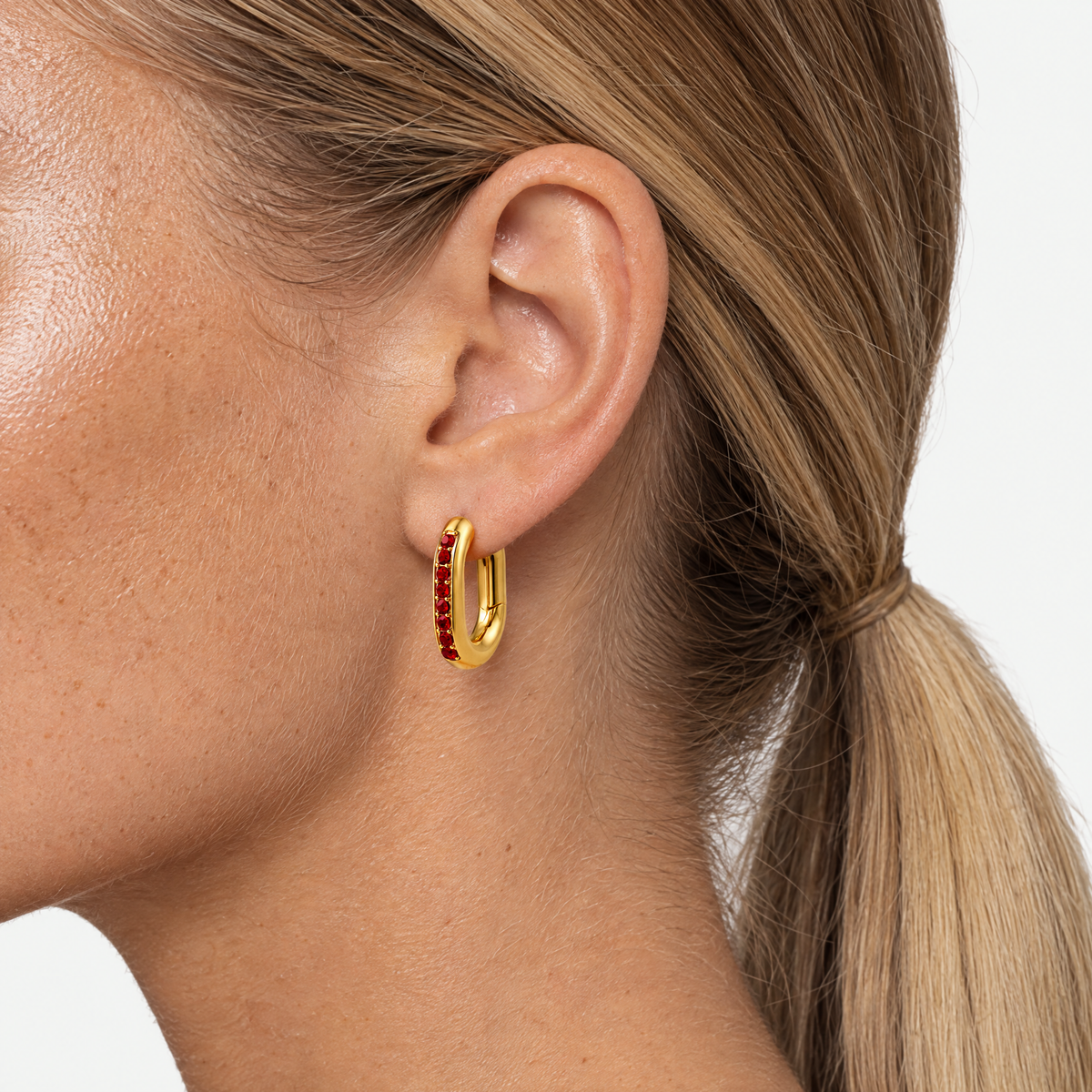 Close up of an ear wearing the oval huggie hoop with red stones
