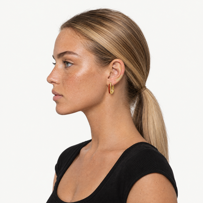 Model wearing the gold-tone oval huggie hoops with red stones