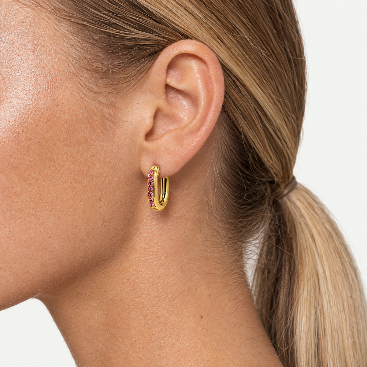 Close up of an ear wearing the oval huggie hoop with pink stones