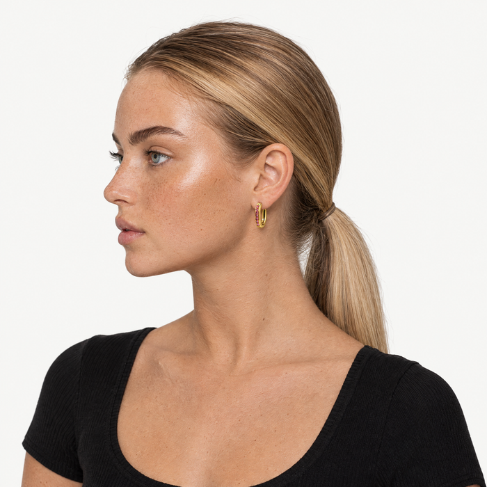 Model wearing the gold-tone oval huggie hoops with pink stones