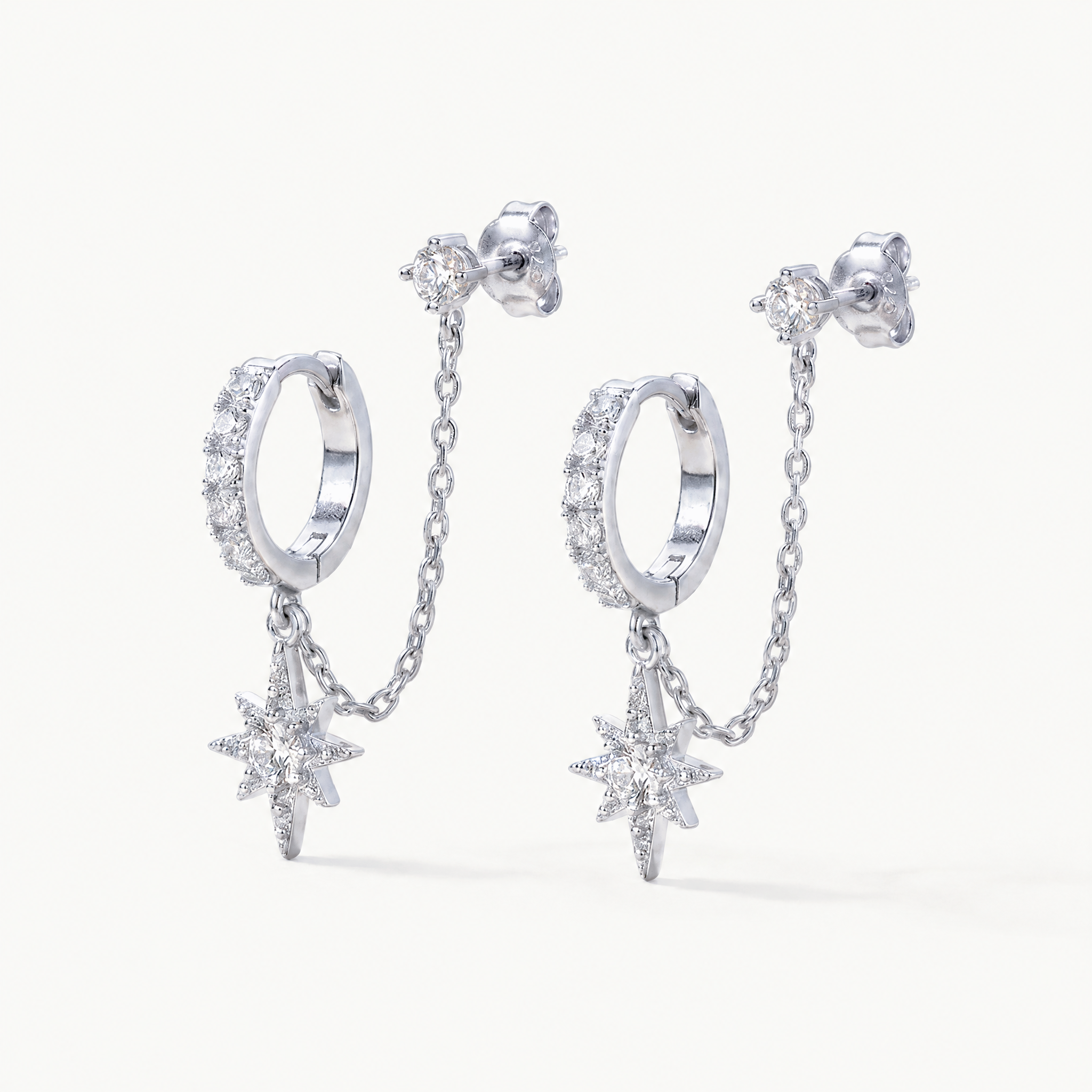 Silver-tone chained huggie earrings with star charm on a light background