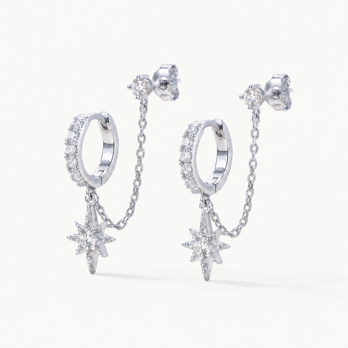 Silver-tone chained huggie earrings with star charm on a light background