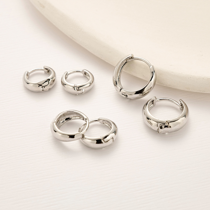Three pairs of silver-tone chunky hoop earrings laid out on a white surface
