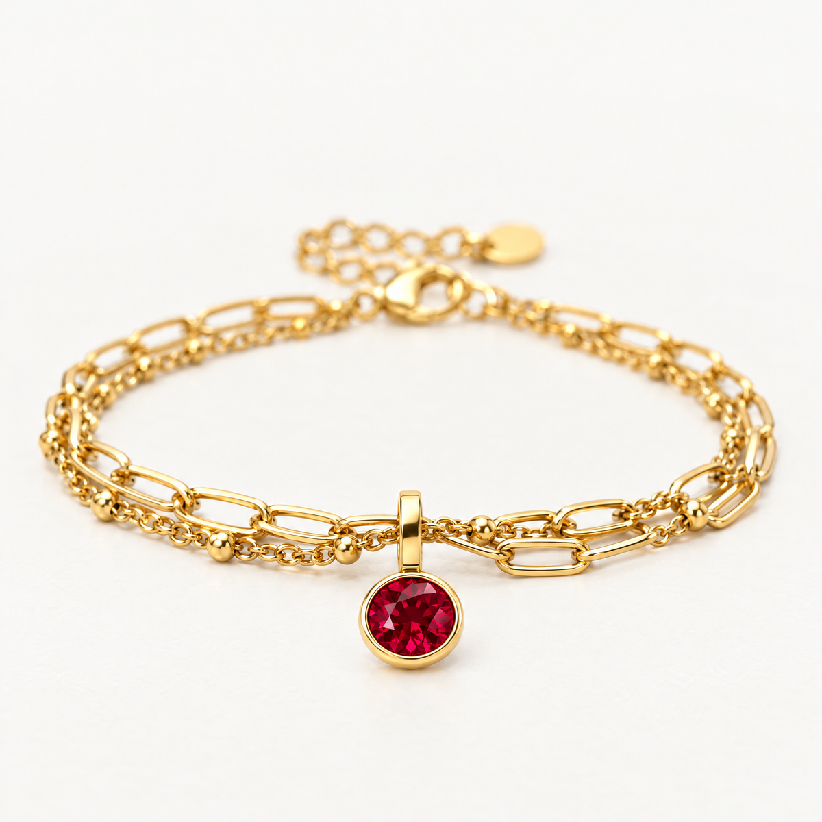 Paperclip chain birthstone bracelet with a round red charm, angled view