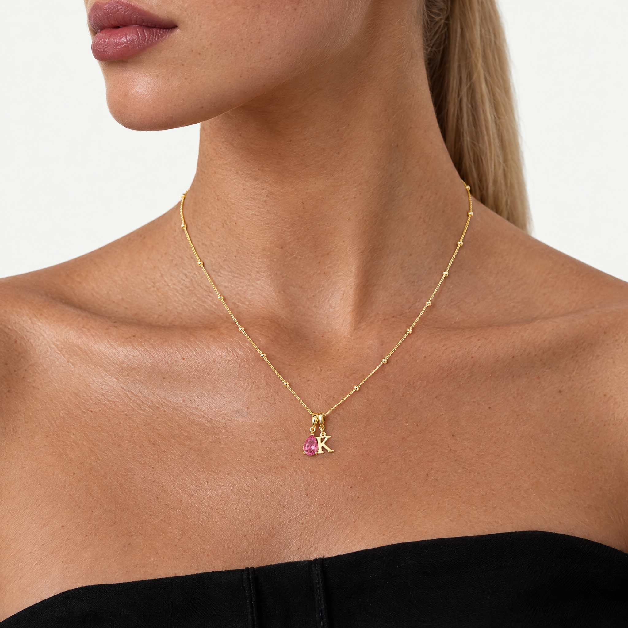 Model wearing the gold-tone initial necklace with letter K and pink crystal teardrop