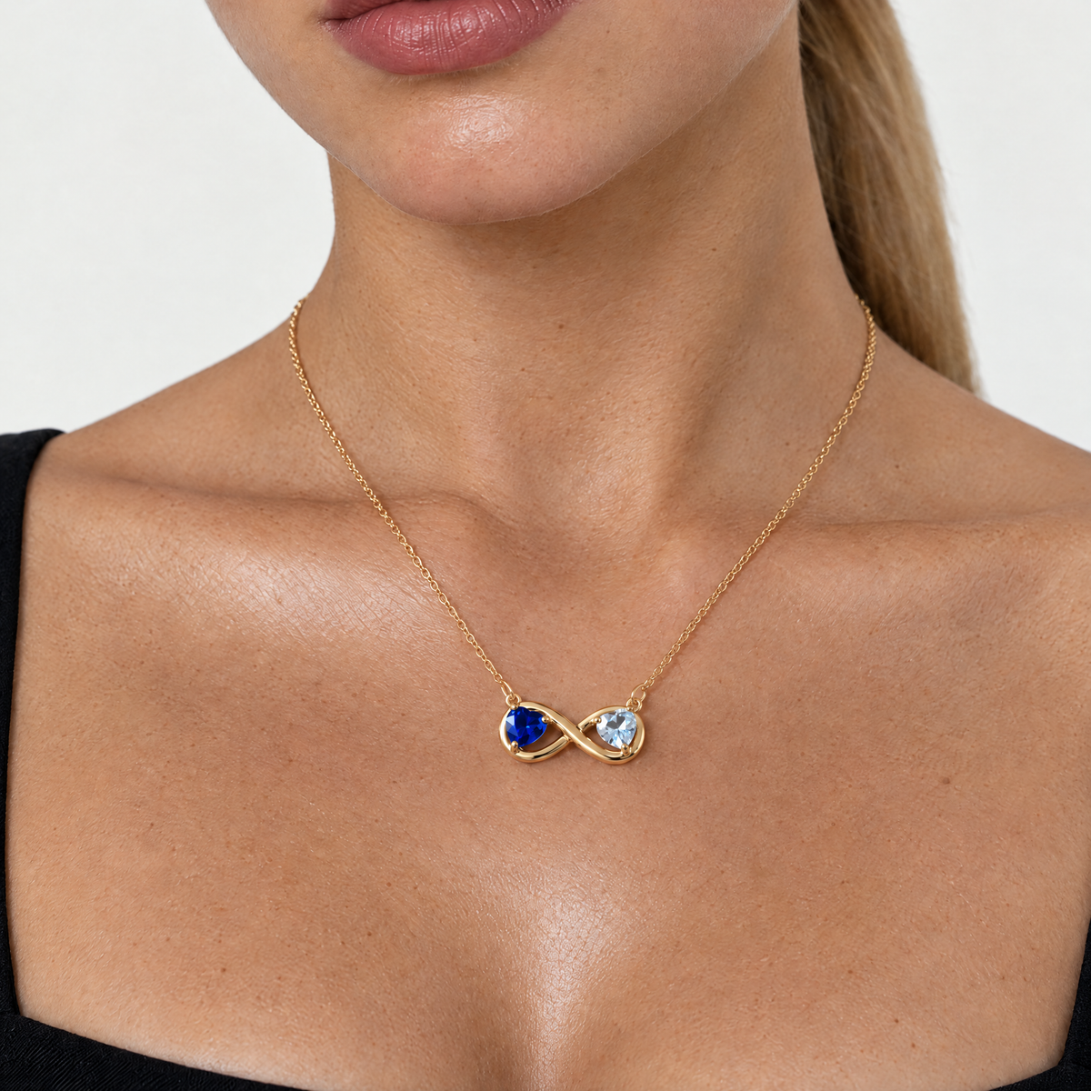 Model wearing the gold-tone infinity necklace with sapphire blue and clear crystal hearts