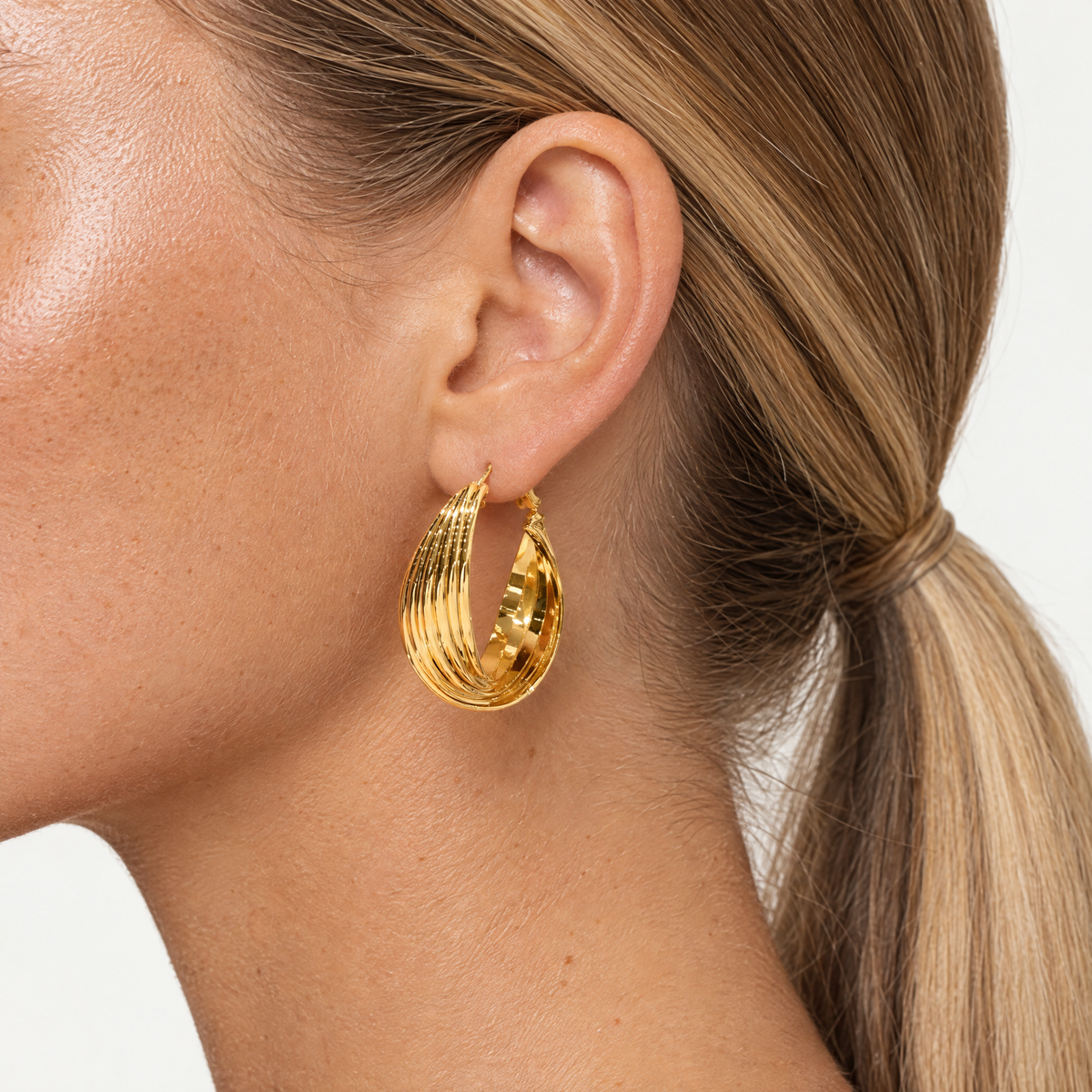 Close up of an ear wearing the gold-tone chunky ribbed hoop earring