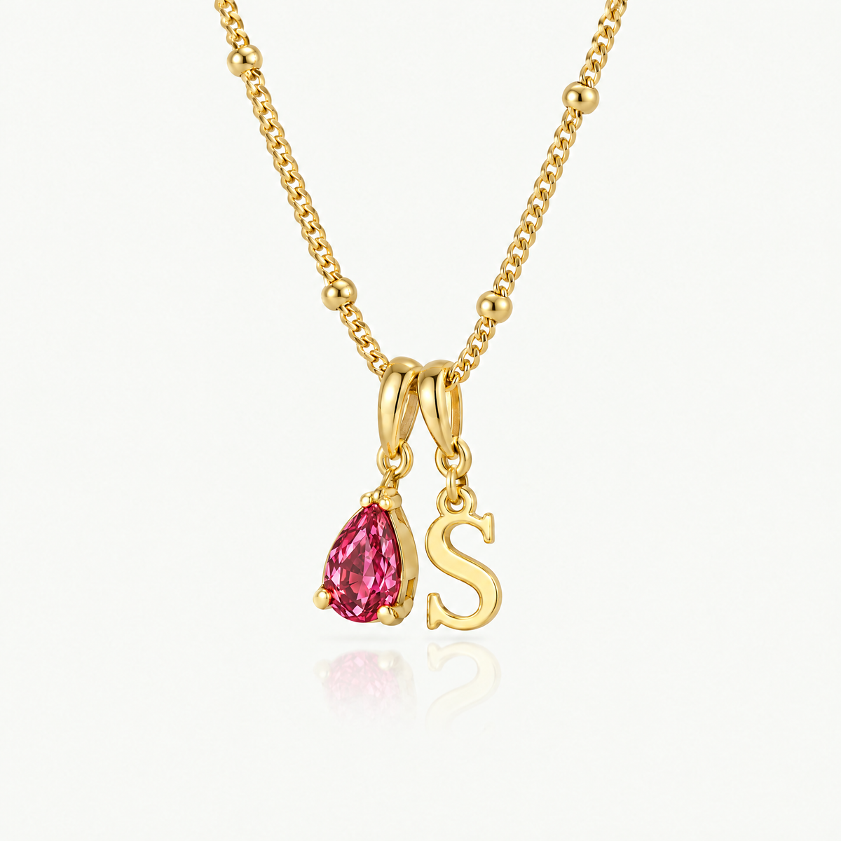 Letter S pendant and pink crystal teardrop on a gold-tone satellite chain, angled view