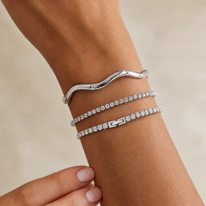 Silver-tone tennis bracelet on the wrist, stacked with other bracelets
