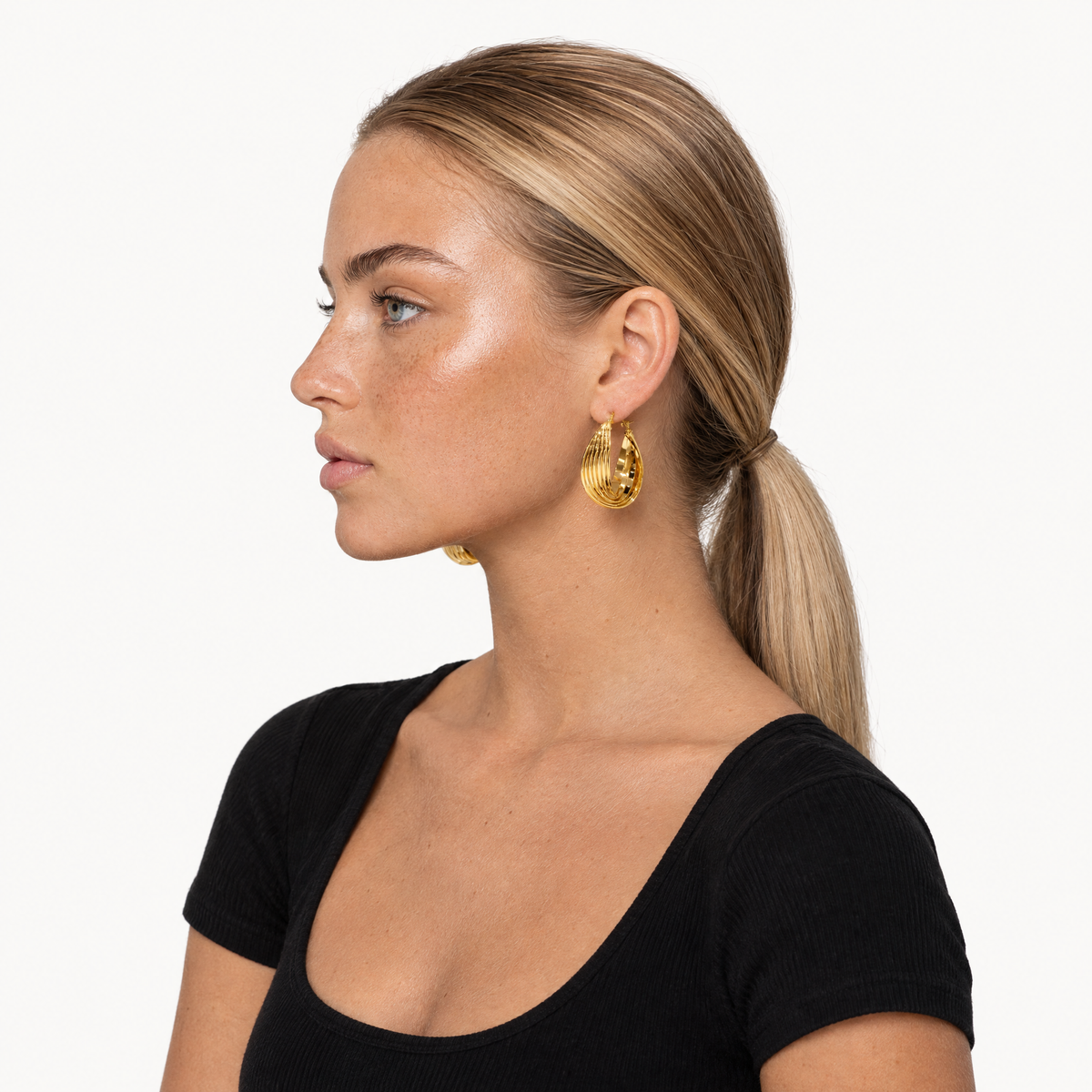 Model in a black top wearing the gold-tone chunky ribbed hoop earrings, side profile