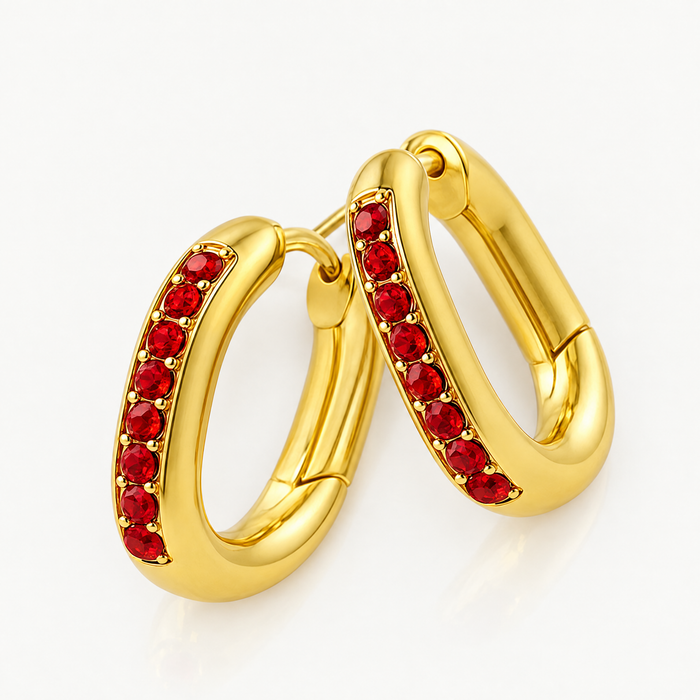 Pair of gold-tone oval huggie hoops with red stones, angled view
