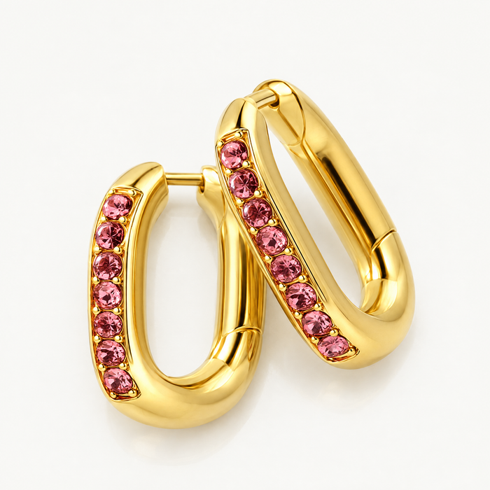 Pair of gold-tone oval huggie hoops with pink stones, angled view